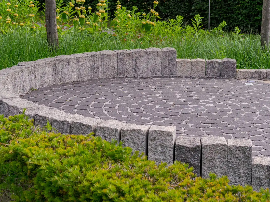 Patio circulaire en pavé uni ceinturé d'un muret et d'une bordure de palissades de granit, entouré de verdure
